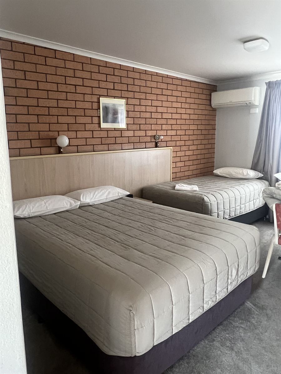 A family room with a queen bed in the foreground and a single bed against the brick wall behind