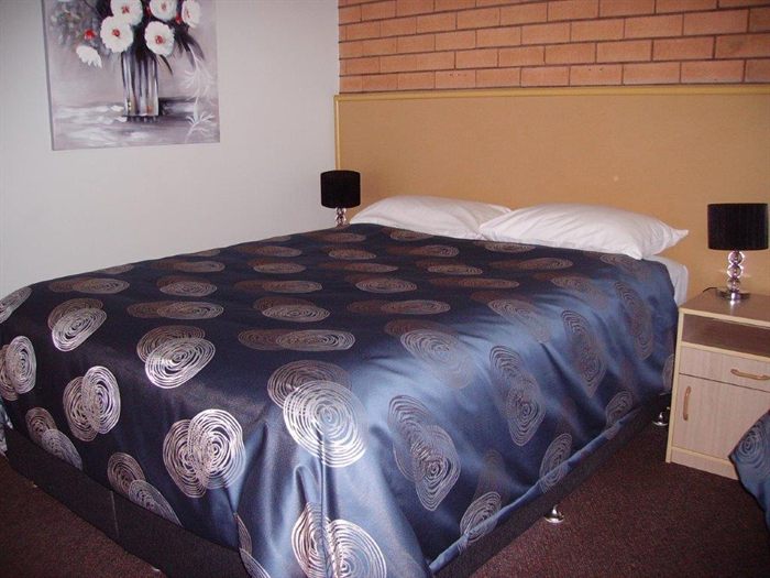 A queen room with a made queen bed, bedside table and lamps