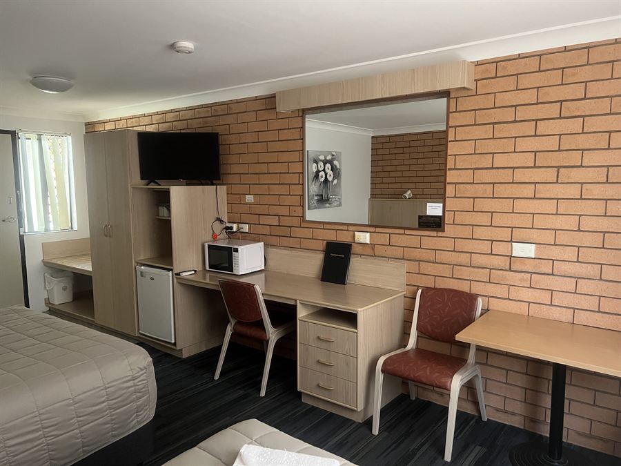 Inside a studio room: desk, bar fridge, microwave and a wall-mounted flat screen television