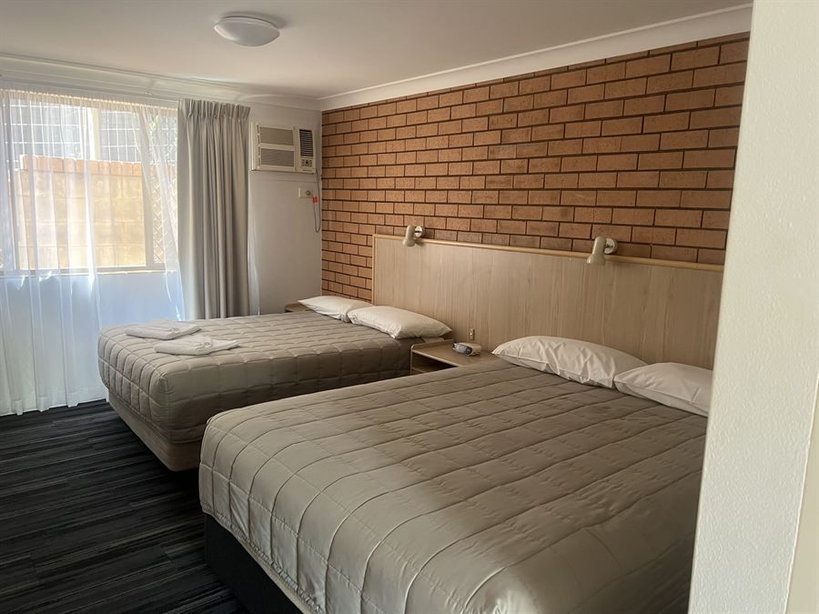 A twin room with two made beds, a timber bedhead and a brick feature wall